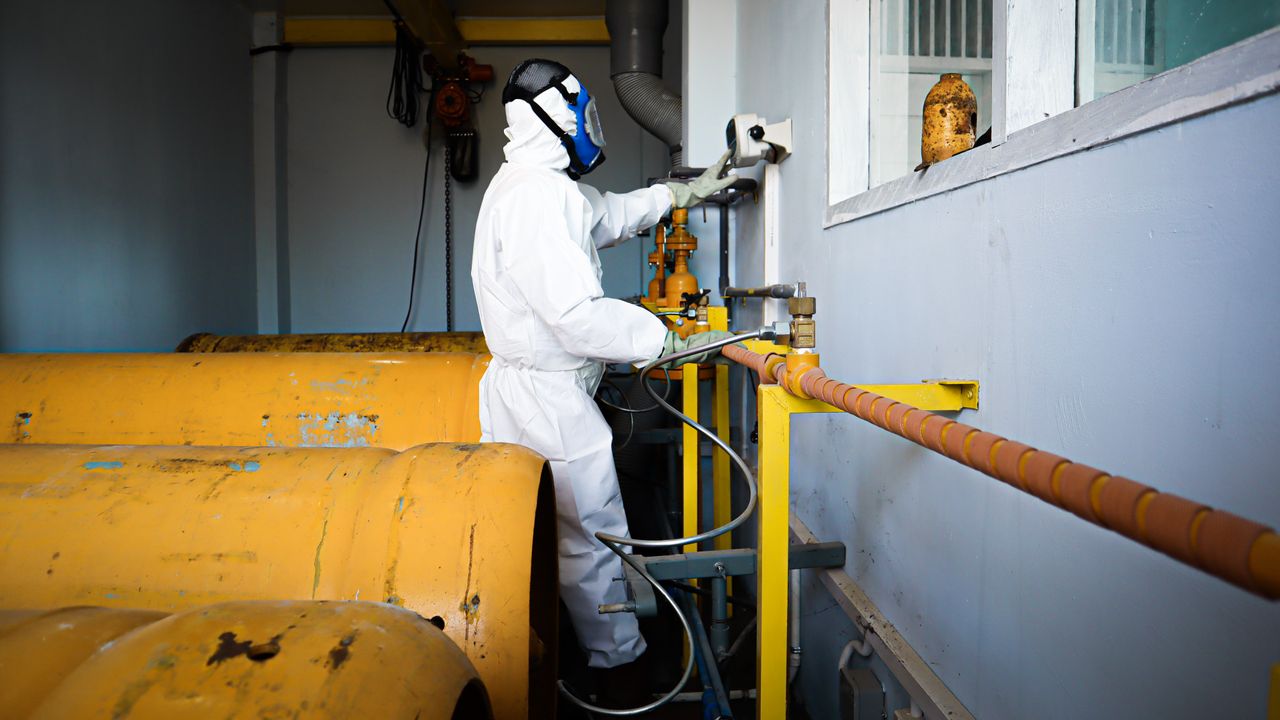 contact-img Worker in full protective suit and gas mask handles industrial pipes indoors in Indonesia.
