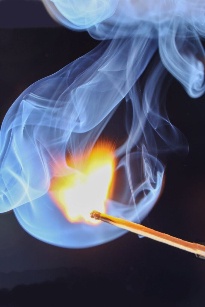 Close-up of a match igniting, creating dramatic smoke patterns on a dark background.