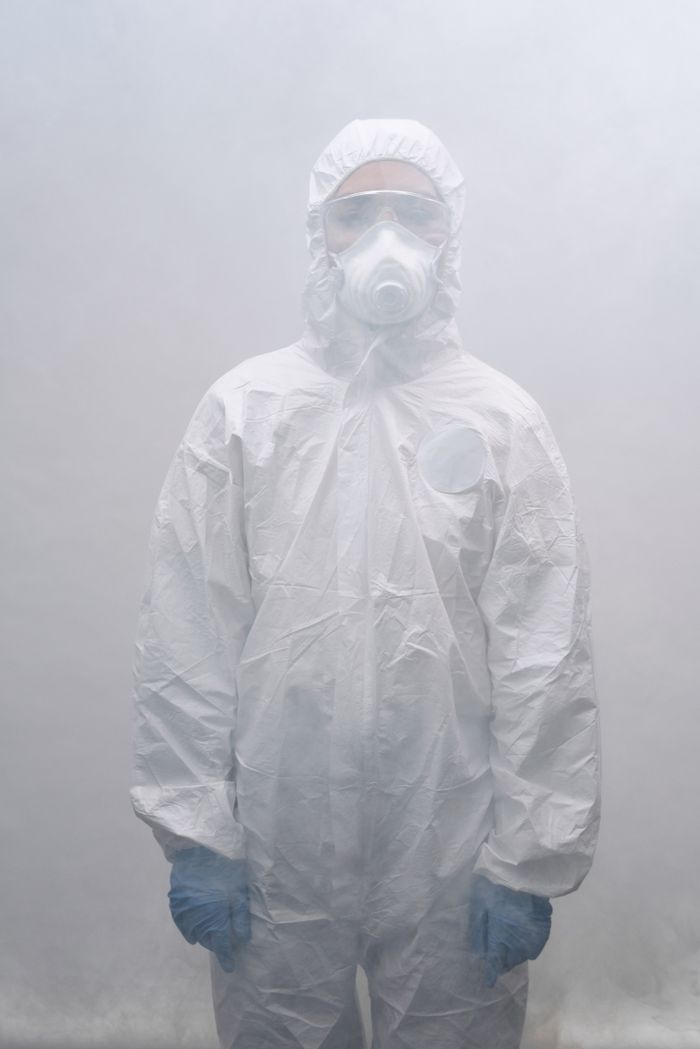 why-choose-us Person in full protective gear with mask standing in foggy environment.