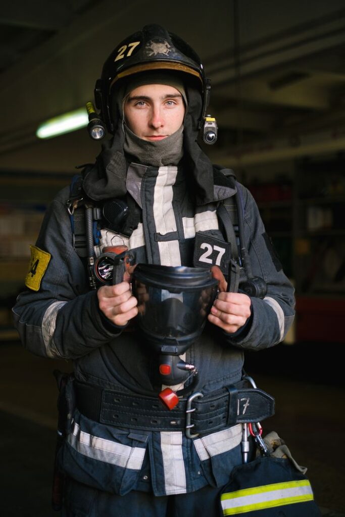 pexels photo 5965194 A focused firefighter holding protective gear indoors, ready for action.